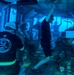This image depicts a U.S. Marine Corps Underwater Egress Training exercise taking place inside a submerged simulator. Multiple personnel in military gear and helmets are practicing emergency escape procedures from a simulated aircraft or vehicle cabin underwater. An instructor wearing a black U.S. Marine Corps 'Ditching - Underwater Egress Trainer' shirt is visible supervising the exercise.