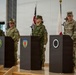 A formal multinational military ceremony featuring personnel from at least three nations standing at podiums in an indoor venue. Three podiums display distinct military unit insignia patches, with flags of Australia, Japan, and the United States visible in the background. The event appears to be a joint military command or coordination ceremony.