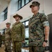 Three military personnel stand at attention in a formal indoor setting, representing at least two different nations' armed forces. The foreground figure wears US Marine Corps MARPAT digital camouflage with visible 'MARINES' tape, while the center figure wears Australian Army multicam uniform with a distinctive wide-brimmed slouch hat. A fourth uniformed individual is partially visible in the background wearing US Army OCP uniform.