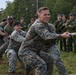 A group of military personnel in US Marine Corps digital camouflage uniforms are competing in a tug-of-war against what appears to be Swedish military personnel wearing woodland camouflage and dark blue berets. The event appears to be a friendly inter-military competition or joint exercise, likely held at a training facility in Scandinavia. Spectators in Swedish military uniforms observe from the sidelines.