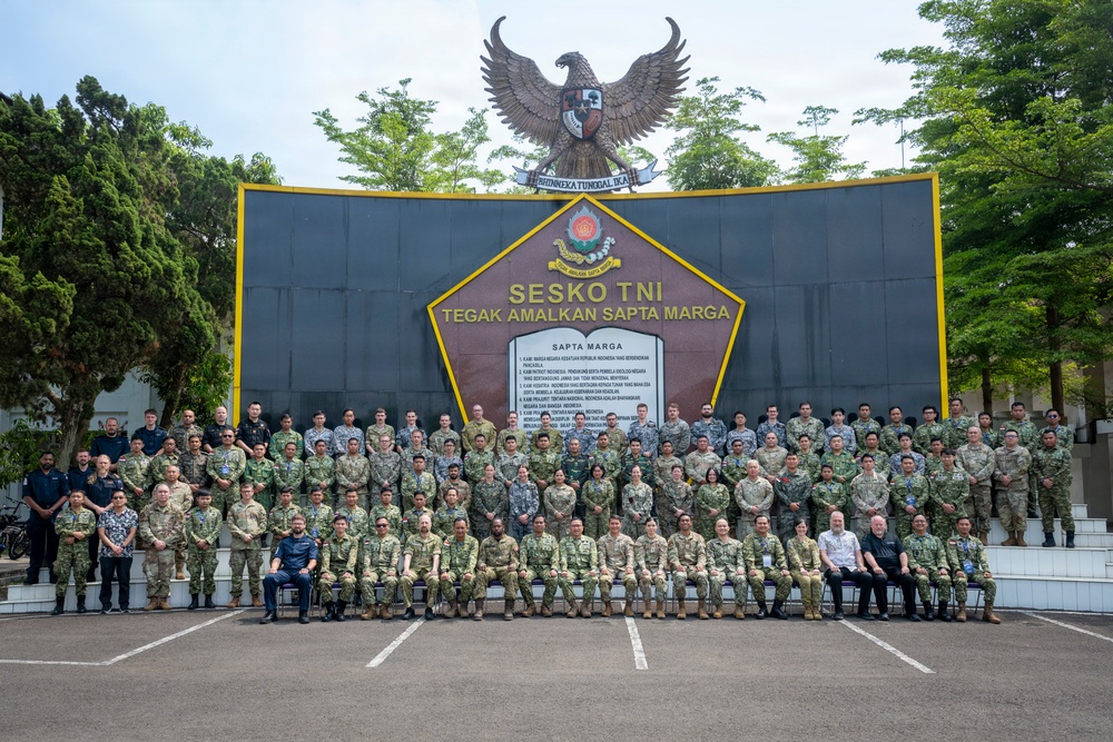 A large group of military personnel from multiple nations pose for a formal group photograph in front of the Sesko TNI (Indonesian Armed Forces Staff and Command School) monument. The backdrop features the Indonesian Garuda Pancasila national emblem atop a dark wall displaying the 'Sapta Marga' (Seven Pledges) military code of conduct. The gathering appears to be a multinational military education or cooperation event.