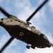 A military medical evacuation (MEDEVAC) helicopter is photographed from directly below as it flies overhead. The aircraft displays red cross markings on its fuselage, identifying it as a medical/rescue helicopter. The image is taken from a ground-up perspective, capturing the underside of the aircraft against a partly cloudy blue sky.