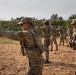 A group of U.S. Army soldiers in OCP (Operational Camouflage Pattern) uniforms are conducting pistol qualification or training on an outdoor firing range. The foreground soldier is actively firing a semi-automatic pistol, with a spent casing visibly ejecting from the weapon. An MP (Military Police) soldier observes from the right side, likely serving as a range safety officer or instructor.