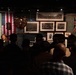 A museum guide or curator is presenting to a group of visitors in front of a dimly lit exhibition display case. The exhibit appears to be titled 'Between the Wars' and features historical football/soccer memorabilia including flags, trophies, and archival photographs. The crowd is gathered closely, listening to the presenter who stands to the left of the display.
