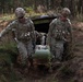 Two U.S. Army soldiers in MultiCam (OCP) uniforms are extracting a simulated casualty on a litter from a field bunker or dugout structure in a forested training area. The soldier on the left is identified by a name tape reading 'LEAVITT.' This appears to be a tactical combat casualty care (TCCC) or medevac training exercise.