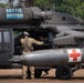 A military medical evacuation (MEDEVAC) helicopter, specifically a UH-60 Black Hawk, is shown on the ground with the callsign 'Arctic Dustoff' painted on its fuselage. The aircraft bears Red Cross markings on both sides, identifying it as a medical helicopter. At least two personnel in military camouflage uniforms and flight helmets are visible, with one appearing to conduct pre-flight checks or maintenance at the cabin door.