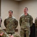 A group of U.S. Army soldiers in OCP (Operational Camouflage Pattern) uniforms are standing at attention or parade rest in what appears to be an indoor briefing or formation setting. Visible name tapes identify at least three soldiers: PETERLIN, NELSON, and a partially visible name ending in '-AMMAD'. One soldier appears to be speaking or addressing someone seated in the foreground.