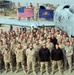 A large group of military personnel pose for a unit photo in front of an A-10 Thunderbolt II (Warthog) attack aircraft bearing the tail number 659. Four individuals standing on the aircraft's wing hold an American flag and what appears to be a Pennsylvania state flag. The setting appears to be a forward operating base in a desert environment, likely during Operation Iraqi Freedom or Operation Enduring Freedom.