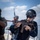Allies, partners train together during Phoenix Express 2026 The image shows personnel conducting what appears to be a maritime security training exercise on the deck of a naval vessel. The primary subject is wearing all-black tactical gear including a helmet and sunglasses, aiming a weapon with orange/red training markings. Additional personnel in mixed military uniforms are visible in the background.