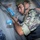 Allies, partners train together during Phoenix Express 2026 A soldier in camouflage uniform and helmet is conducting what appears to be a military training exercise, holding a rifle with blue-painted components indicating simunition or training ammunition. He is positioned against a metal wall in a tactical stance, with another person in blue digital camouflage visible nearby. The blue markings on the weapon and magazine are consistent with training/exercise equipment used to distinguish live weapons from training variants.