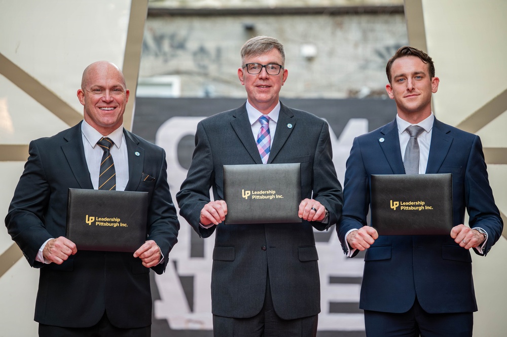 Three men in business suits are posing for a formal photograph while holding black portfolio folders branded with 'Leadership Pittsburgh Inc.' in gold lettering. The setting appears to be an indoor venue with a decorative backdrop. This appears to be a graduation or recognition ceremony for the Leadership Pittsburgh Inc. program.