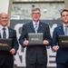 Three men in business suits are posing for a formal photograph while holding black portfolio folders branded with 'Leadership Pittsburgh Inc.' in gold lettering. The setting appears to be an indoor venue with a decorative backdrop. This appears to be a graduation or recognition ceremony for the Leadership Pittsburgh Inc. program.