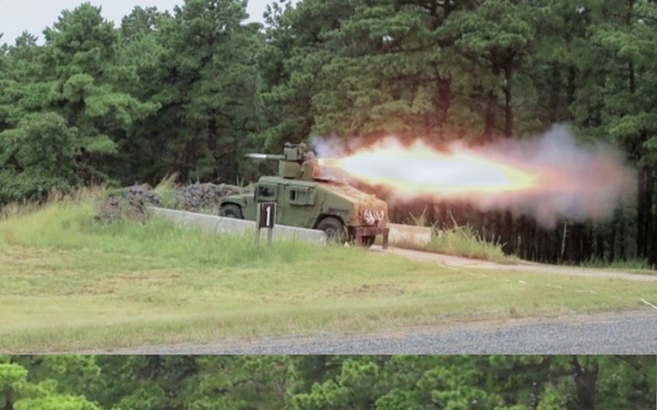 Two sequential photographs show a military HMMWV (Humvee) vehicle firing a missile or rocket from a roof-mounted launcher system. The vehicle, marked with the number '1', is positioned behind a concrete barrier with a sandbag emplacement. The images capture the launch sequence, with the top image showing the initial blast/fireball and the bottom image showing the missile in flight with exhaust trail.