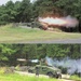 Two sequential photographs show a military HMMWV (Humvee) vehicle firing a missile or rocket from a roof-mounted launcher system. The vehicle, marked with the number '1', is positioned behind a concrete barrier with a sandbag emplacement. The images capture the launch sequence, with the top image showing the initial blast/fireball and the bottom image showing the missile in flight with exhaust trail.