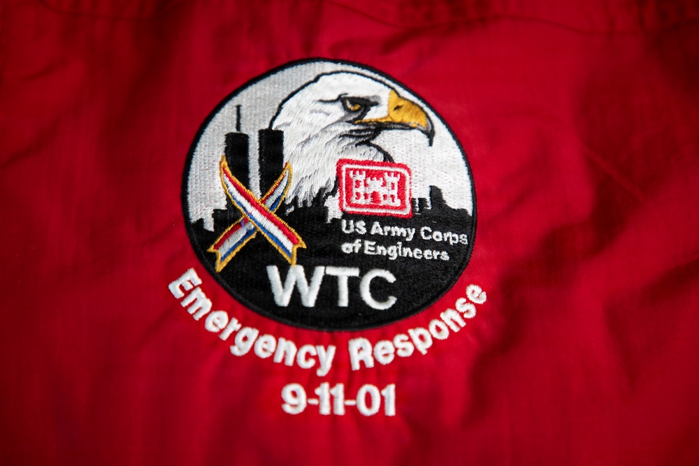 The image shows an embroidered patch on a red jacket or garment commemorating the US Army Corps of Engineers' emergency response to the World Trade Center on September 11, 2001. The circular patch features a bald eagle, the Twin Towers silhouette, a patriotic ribbon, and the USACE castle logo. Text on the patch reads 'WTC Emergency Response 9-11-01'.