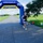 A runner wearing bib number 408 crosses through an inflatable START/FINISH arch at a road race organized by Navy MWR Cape Canaveral. The event takes place on a paved road surrounded by green grass fields under a partly cloudy sky. The runner is dressed in a black tank top, white shorts, white sneakers, and sunglasses.