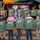A group of approximately 12 people pose for a congratulatory photo, each holding up olive/army green sweatshirts with a graphic design reading 'Lighting the Way to Success 450' with what appears to be an electrician/utility themed logo. Gold number balloons spelling '2026' flank a screen displaying 'CONGRATULATIONS' in the background. The event appears to be a graduation or program completion ceremony.