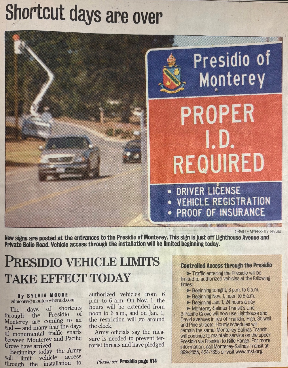 A newspaper article titled 'Shortcut days are over' covers new vehicle access restrictions at the Presidio of Monterey military installation. The article, written by Sylvia Moore for the Monterey Herald, announces that the Army is implementing controlled vehicle access to prevent terrorist threats. A photograph shows a 'Proper I.D. Required' sign at the Lighthouse Avenue and Private Bolio Road entrance, listing driver license, vehicle registration, and proof of insurance as required documents.