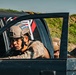 The image shows military personnel riding in tactical vehicles, wearing combat helmets and camouflage uniforms. At least two nations are identifiable from helmet patches: El Salvador (visible on the foreground soldier's helmet) and what appears to be Paraguay (text visible on a flag/banner inside the vehicle). The scene appears to be a military exercise or convoy operation.