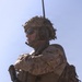 A heavily equipped military service member is photographed from a low angle against a clear blue sky. The soldier is wearing desert camouflage (MARPAT pattern consistent with USMC), full tactical gear, and is carrying a rifle. The image is dramatically lit with strong backlighting, emphasizing the silhouette and equipment of the subject.