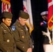 Two U.S. Army officers in Army Green Service Uniforms stand with heads bowed during what appears to be a formal military ceremony. The female officer on the left wears a brigadier general star and name tape reading 'McDENEGAL,' while the male officer on the right displays Airborne and 18th Airborne Corps patches with name tape reading 'EBBERT.' Multiple military flags and a color guard are visible in the background.