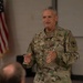 A U.S. Army Major General named Jones, identifiable by two stars on his collar and the name tape on his uniform, is addressing an audience in what appears to be a briefing or meeting room. He is wearing the Operational Camouflage Pattern (OCP) uniform with a unit patch on his left shoulder. An American flag is visible in the background.
