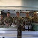Five U.S. Army soldiers in OCP (Operational Camouflage Pattern) uniforms are posing together behind a military field kitchen serving line. They appear to be food service personnel (cooks/92G MOS) staffing a mobile kitchen trailer (MKT). The soldiers are smiling for what appears to be an official or informal group photo.