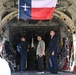 The image shows the interior of a large military cargo aircraft, likely a C-130 Hercules, with several civilians and at least one military personnel standing inside the open cargo bay. A modified Texas state flag featuring a C-130 aircraft silhouette in place of the lone star is prominently displayed hanging from the ceiling. The setting appears to be an airshow or public tour event based on the civilian attire and informal atmosphere.
