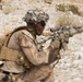 A soldier in desert camouflage uniform is captured in motion while aiming a rifle equipped with an optical scope. The image uses a radial blur/zoom effect centered on the subject, creating a sense of dynamic movement. A second figure is faintly visible in the background on elevated terrain.