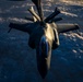 An aerial refueling operation is captured from above, showing a fighter jet — consistent with an F-35 Lightning II — receiving fuel from a tanker aircraft via a boom refueling system. The image is taken from the tanker's perspective looking down at the receiving aircraft, with a dramatic cloud layer visible far below. The letters 'ANG' (Air National Guard) are visible on the refueling boom.