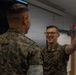 Two U.S. Marines in MARPAT camouflage uniforms are engaged in a conversation inside what appears to be a briefing or classroom environment. The Marine facing the camera is smiling broadly and holding up one finger, possibly making a point or emphasizing something during the discussion. The setting suggests a training or operational planning context.
