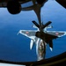 An aerial refueling operation is captured from the boom operator's window of a tanker aircraft, showing a Japan Air Self-Defense Force (JASDF) F-2 fighter jet receiving fuel via a flying boom. The F-2 aircraft displays distinctive Japanese roundel markings (red circles) on its wings and fuselage. The deep blue ocean is visible far below, indicating high-altitude flight.