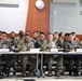A group of military personnel from what appears to be a joint U.S. Army and Republic of Korea (ROK) Army meeting or briefing session, seated at conference tables in a modern indoor facility. The soldiers are smiling and appear engaged in a positive, collaborative atmosphere. Name placards are visible on the tables, suggesting a formal but friendly exchange or training event.