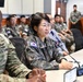 A joint military meeting or briefing is taking place between U.S. Army and Republic of Korea (ROK) Army personnel. A female ROK Army officer wearing a general's star insignia is speaking at a conference table equipped with microphones and name placards. The setting appears to be a formal military conference room with both nations' service members seated in attendance.