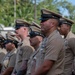 A group of United States Navy Chief Petty Officers standing in formation at what appears to be an outdoor military ceremony. The personnel are wearing the Navy Service Uniform (NSU) in tan/khaki with combination covers (peaked caps). The setting appears to be in a tropical location based on the palm trees visible in the background.