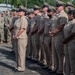 A formal military ceremony featuring U.S. Navy personnel in khaki service uniforms standing at attention in organized formation. In the background, additional military personnel in Army combat uniforms (ACUs) are also present, suggesting a joint-service event. The setting appears to be an outdoor parade ground or courtyard, likely at a military installation in a tropical location.