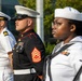 The image shows a formal military ceremony featuring personnel from multiple U.S. armed service branches standing at attention. Visible are a U.S. Navy officer in dress whites, a U.S. Marine Corps Staff Non-Commissioned Officer in dress blues, and two U.S. Navy enlisted sailors in their dress white uniforms. The setting appears to be an outdoor ceremonial event, likely a parade, memorial, or official military observance.
