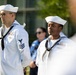 Two U.S. Navy sailors in dress white uniforms stand at attention during what appears to be a formal military ceremony or event. The sailor on the left displays Petty Officer rating chevrons and multiple service ribbons, while the sailor on the right also wears ribbons and a qualification badge. Both wear the traditional white Dixie cup covers and black neckerchiefs.