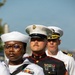 Three U.S. military personnel in dress uniforms are standing in formation, likely during a formal ceremony or parade. The group includes a U.S. Navy enlisted sailor (foreground), a U.S. Marine Corps Staff Non-Commissioned Officer in dress blues (center), and a U.S. Navy officer (background). All individuals are wearing service medals and ribbons, indicating experienced service members.