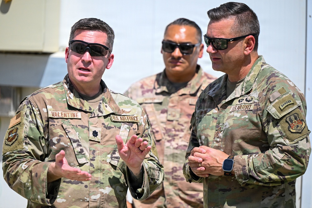 Three U.S. Air Force personnel in OCP (Operational Camouflage Pattern) uniforms are engaged in conversation outdoors in what appears to be a bright, sunny environment. The individual on the left, identified by his name tape as 'Valentine,' holds the rank of Lieutenant Colonel (oak leaf cluster visible) and appears to be briefing or explaining something. The person on the right wears a 'Ranger' tab and U.S. Air Force insignia, while a third individual stands in the background.