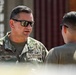 Two U.S. Air Force personnel are engaged in a conversation outdoors near what appear to be shipping containers. The individual facing the camera wears OCP (Operational Camouflage Pattern) uniform with a name tape reading 'WILFONG' and a 'U.S. AIR FORCE' branch tape, along with visible qualification badges. Both individuals are wearing sunglasses, suggesting bright outdoor conditions.