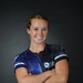A portrait photograph of a person wearing a United States Space Force athletic jersey combined with military camouflage (MultiCam) trousers and a tan rigger's belt. The subject is posed with arms crossed and smiling against a dark studio background. The image appears to be an official or semi-official military sports portrait.