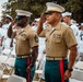 A military ceremony featuring United States Marine Corps personnel in the foreground saluting, wearing Service Charlie uniforms with green trousers and red blood stripes. Behind them, a large formation of U.S. Navy sailors in white dress uniforms are also saluting. The setting appears to be an outdoor ceremonial event, likely a change of command, retirement, or memorial service.
