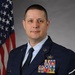 A formal military portrait of a United States Air Force enlisted member in dress blue uniform. The subject displays numerous service ribbons, badges, and rank insignia consistent with a senior non-commissioned officer. An American flag is visible in the background, typical of official military portrait settings.