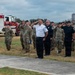 A formal outdoor ceremony showing military personnel in camouflage uniforms and civilian first responders rendering salutes together. A Fire Rescue truck bearing a United States Air Force emblem is visible in the background, suggesting this is a military installation ceremony. The gathering appears to be a memorial or commemorative event involving both military and civilian emergency services personnel.