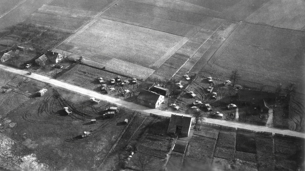 A black-and-white aerial photograph showing a rural crossroads settlement surrounded by agricultural fields. Multiple military or heavy vehicles are visible clustered around a road intersection with several farm buildings. The image appears to be a wartime or mid-20th century reconnaissance photograph based on its style and content.