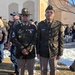 Two U.S. Army soldiers in Army Green Service Uniforms (Class A) are standing together outdoors, likely at a military ceremony or graduation event. The soldier on the left wears a drill sergeant hat and displays multiple service ribbons and a nameplate reading 'JOHNSON' with Staff Sergeant rank insignia. The soldier on the right wears a garrison cap with nameplate reading 'BIBILONI' and a belt with the older-style uniform configuration.