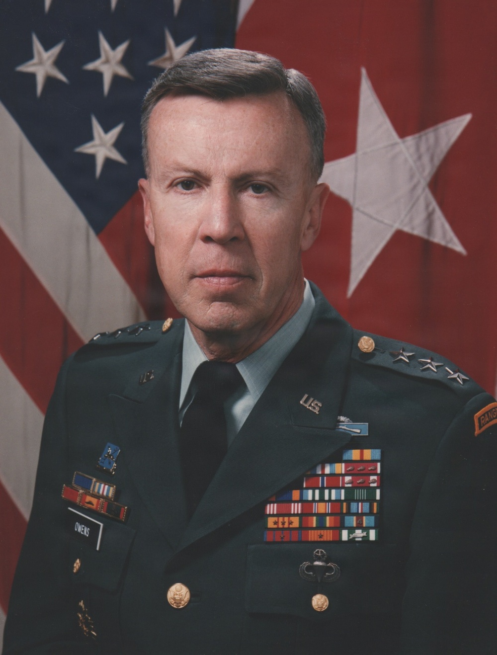 A formal U.S. Army official portrait of a senior general officer in dress green uniform. The subject is identified by a name tag reading 'OWENS' and wears two-star (Major General) rank insignia on the shoulder boards. He is posed in front of the U.S. national flag and a red two-star general officer flag.