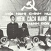 A black-and-white photograph showing a political meeting or indoctrination session held under a communist banner with hammer and sickle symbol. The banner text in Vietnamese reads 'Hội Nghị Chính Huấn' (Political Training Conference) and references 'Đoàn Thanh Niên Cách Mạng Nhân Dân' (People's Revolutionary Youth Union) at 'Mỹ Thạnh Đông'. Several young Vietnamese individuals are seated and standing around a table in what appears to be a formal organizational gathering.