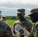 Several U.S. Army soldiers in OCP (Operational Camouflage Pattern) uniforms are gathered outdoors, engaged in conversation at what appears to be a shooting range. One soldier is holding a paper shooting target with a bullseye pattern. The setting appears to be a training exercise or qualification event in a rural, open field environment.